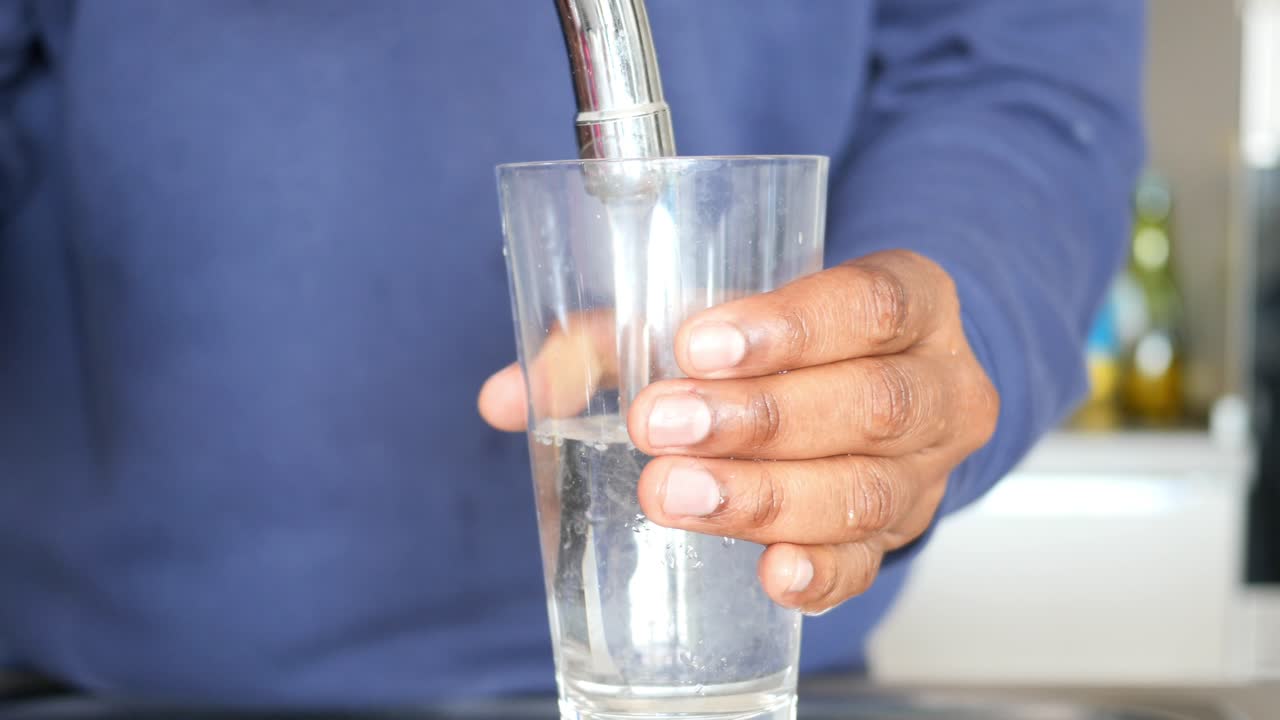 주방 프에서 물로 유리잔을 채우는 사람