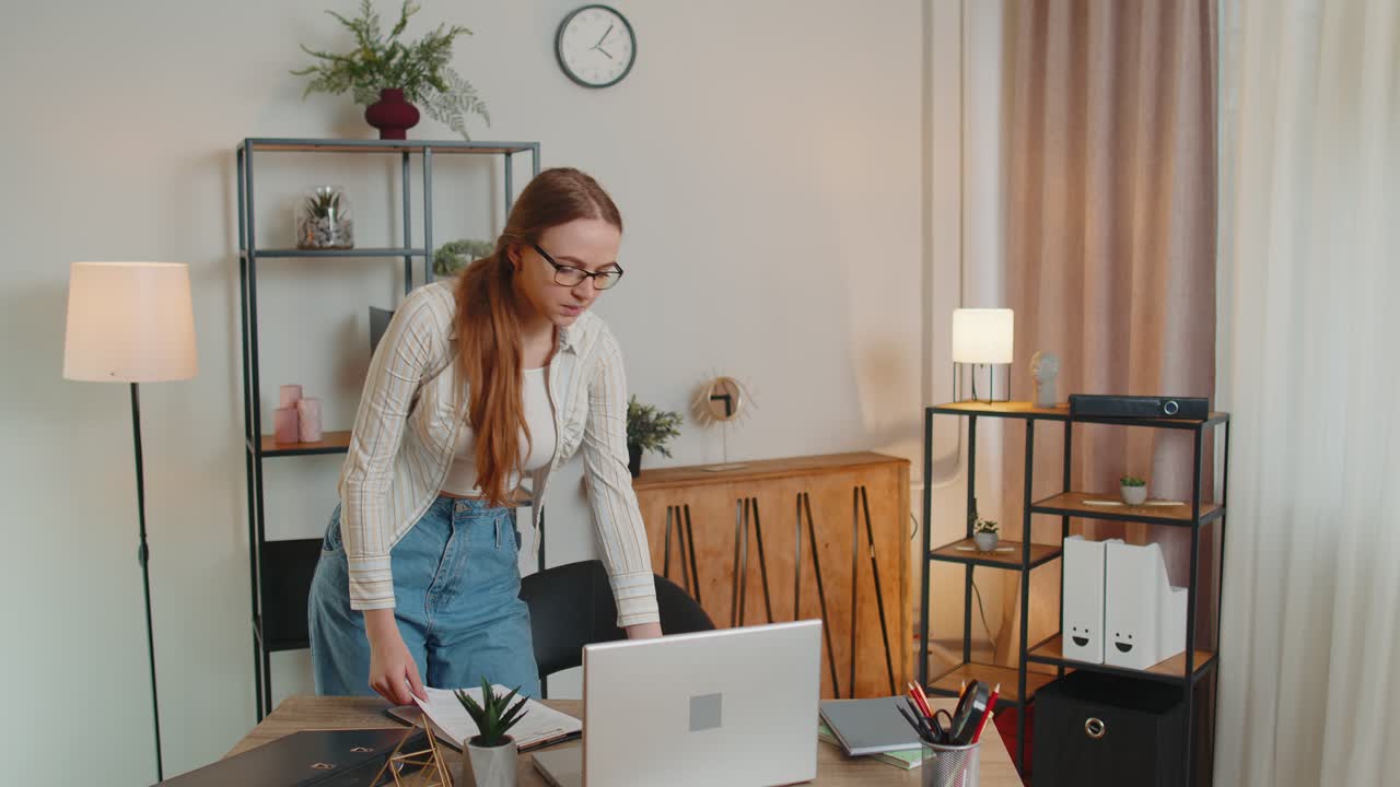 Young woman girl standing by desk in home office working at paper documents analyzes checks data