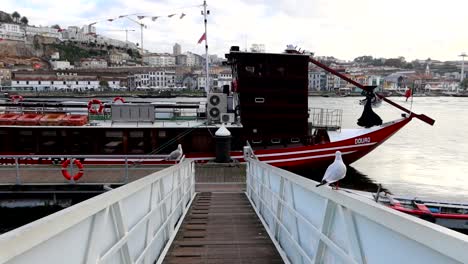 Seagulls-take-flight-near-Rabelo-boat-on-ramp-next-to-Douro-River,-Porto