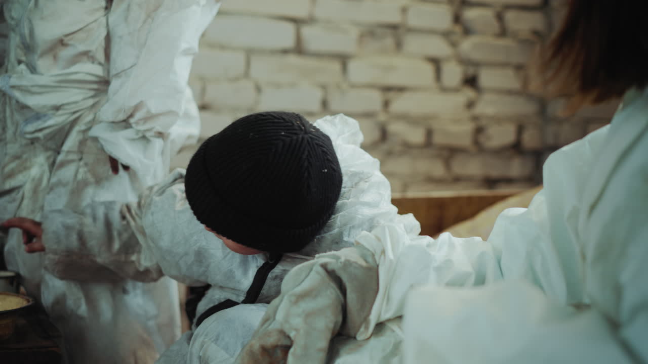 Refugee child dressed in worn protective clothing looks with curiosity while talking to adult beside him in shelter, highlighting innocence, hardship, and human connection