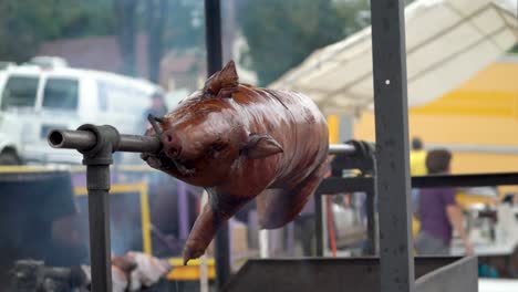 wide shot of a pig turning on a spit over a barbecue at a festival