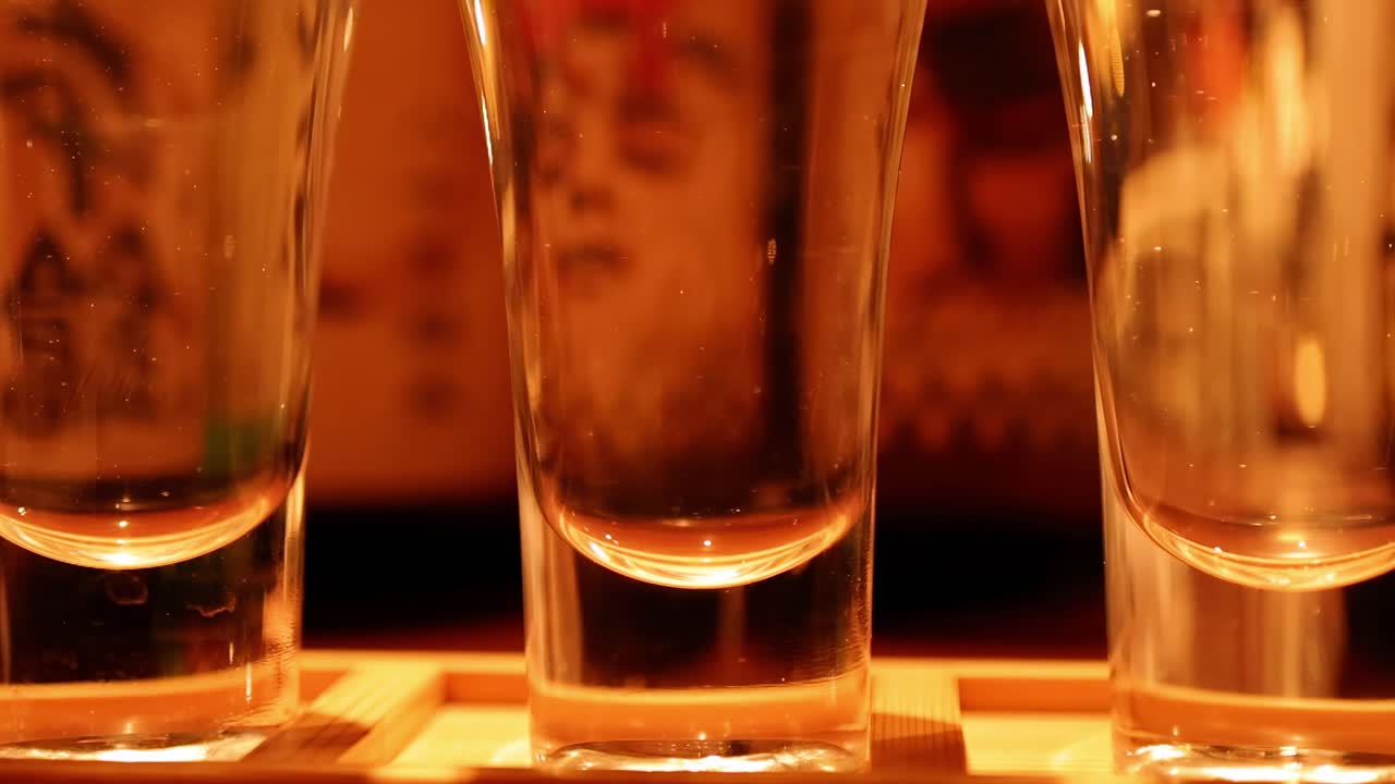 A series of clear glasses on a wooden surface, illuminated by warm ambient lighting.