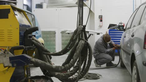 african american male car mechanic wearing a face mask and polishing a side of a car with a grinder