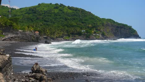 Tiro-Completo,-Un-Surfista-Sale-De-La-Playa-En-Un-Día-Soleado-En-La-Playa-De-Bitcoin-En-El-Salvador,-México,-Vista-Panorámica-De-La-Playa-Y-El-Acantilado-En-El-Fondo