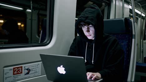 a young adult types away on their laptop while seated on a train traveling through the city during the late hours of the night