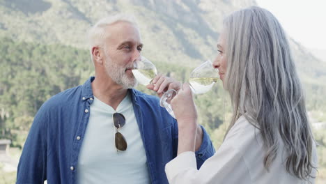 Feliz-Pareja-Caucásica-De-Mediana-Edad-Bebiendo-Vino-En-La-Terraza-De-Las-Montañas,-Cámara-Lenta