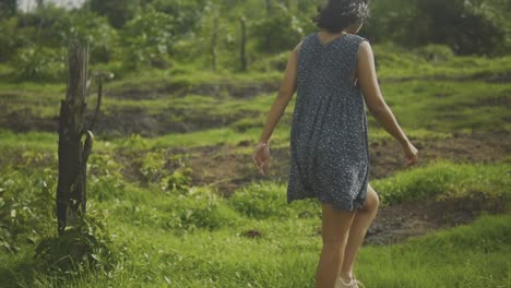 Female-model-with-black-hair-wearing-flowing-blue-dress-and-white-trainers-walking-up-steep-grassy-hill