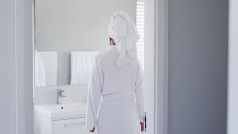 african american woman in bathrobe touching her face looking in the mirror at bathroom