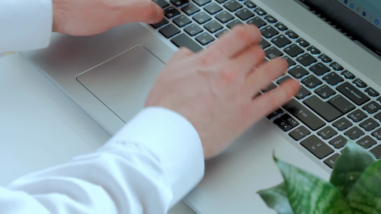 A man in a white shirt is working at a laptop top view. Close-up