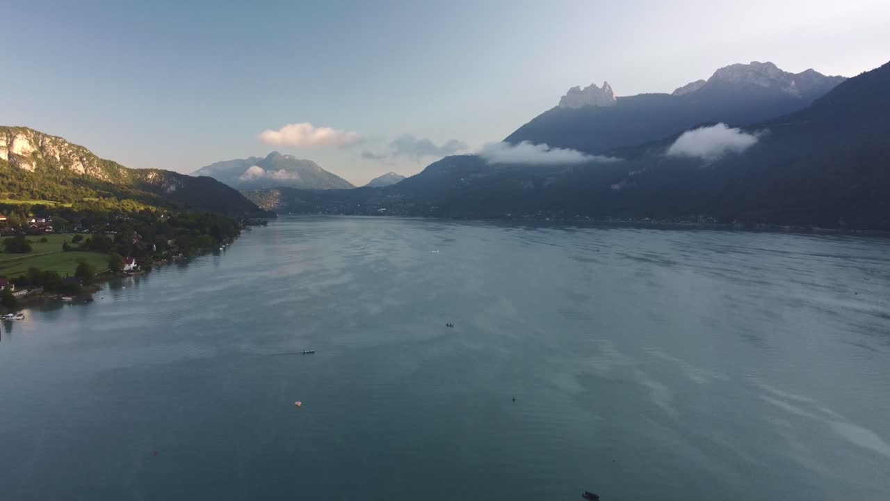 Lake Annecy aerial view at sunrise. A shot up the lake with clouds resting on the mountains the far side. Recorded at sunrise as the sun just appears over the top of the mountains