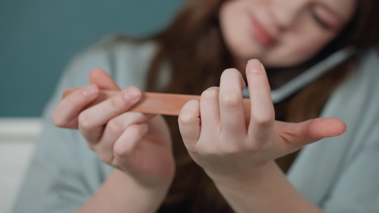 Female individual polishing her nails carefully. Young woman preparing her nails in studio bedroom setting. Youthful woman focusing on precise cuticle and nail grooming in cozy room