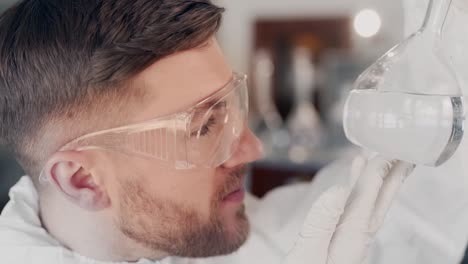 closeup portrait of scientist man in protective suit and glasses examines flask with water