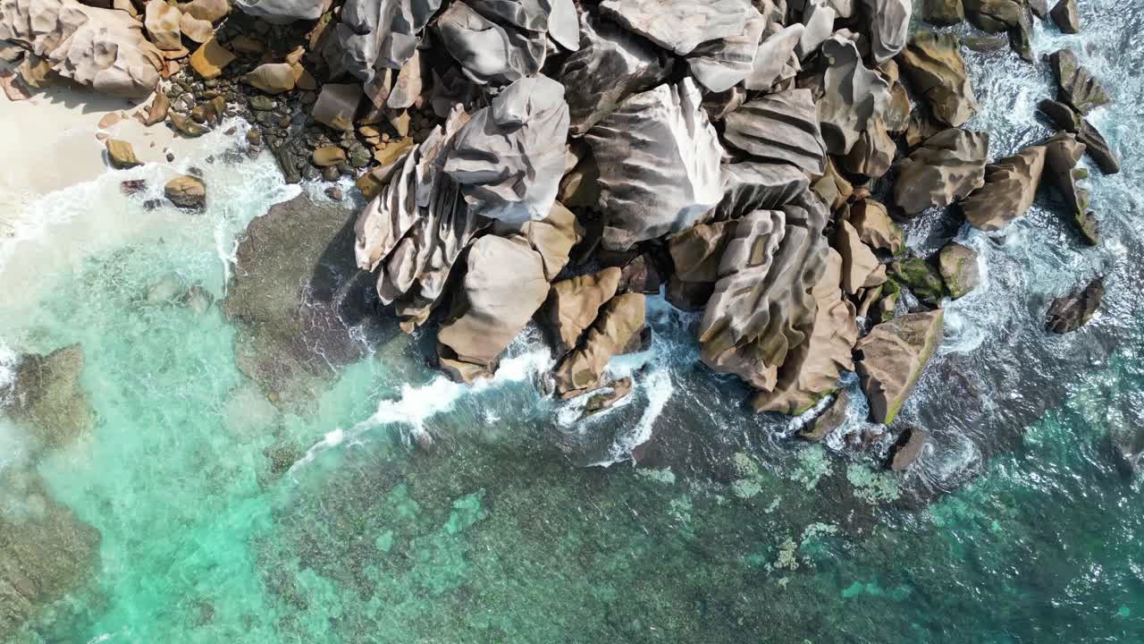 Zoom aereo dall'alto di onde che si infrangono su una spiaggia rocciosa nell'arcipelago delle Seychelles, isola di La Digue.