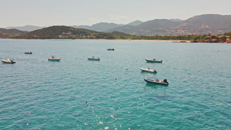 Grupo-De-Barcos-Amarrados-En-Las-Aguas-Azules-Tropicales-Durante-Un-Día-Soleado-En-Cerdeña,-Italia---Tiro-Aéreo,-Estático