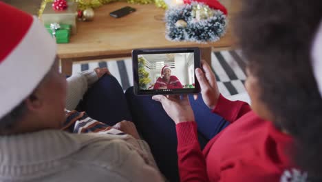 African-american-mother-and-daughter-using-tablet-for-christmas-video-call-with-friend-on-screen