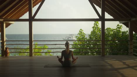 woman sitting in yoga easy pose meditating to soothing ocean sound in private outdoor patio