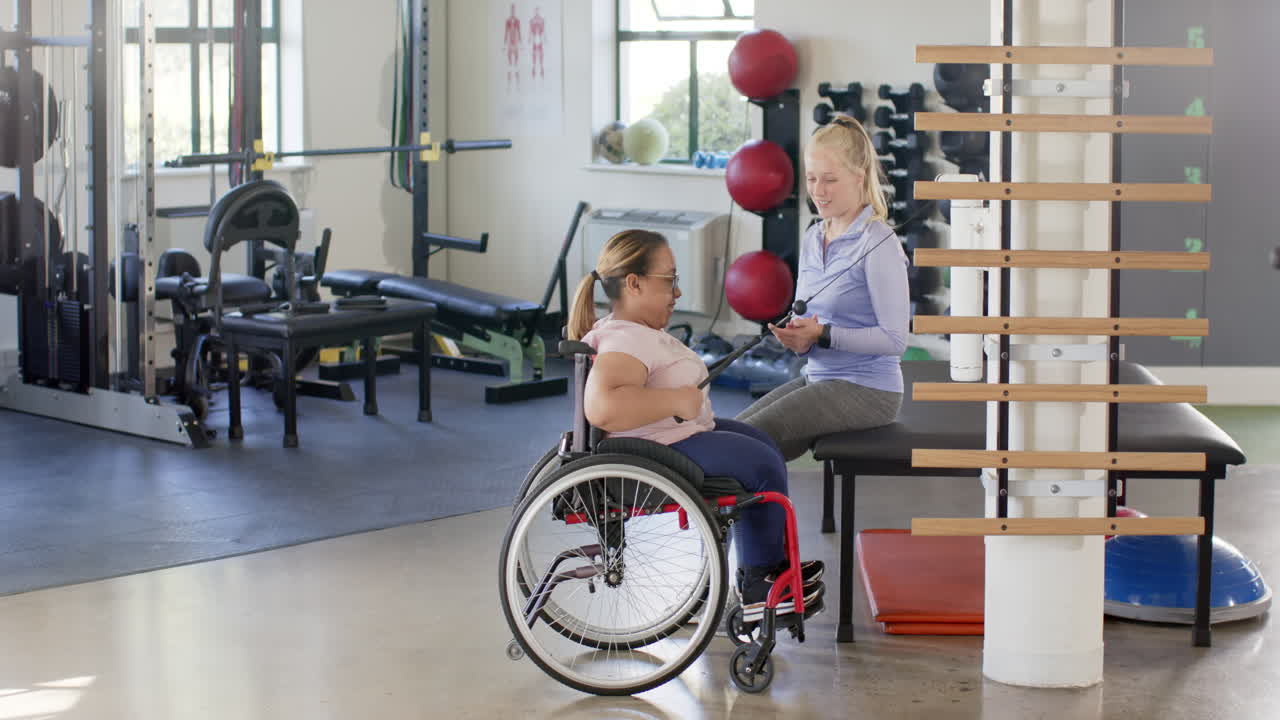 In rehabilitation center, woman with paraplegia in wheelchair exercising, resistance band, therapist