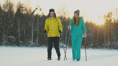 a man in a yellow jacket and a girl in a blue jumpsuit skiing in slow motion at sunset