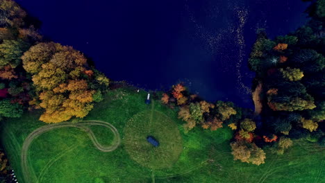 Toma-Aérea-Superior-Sobre-Una-Cabaña-Rectangular-Junto-A-Un-Lago-Prístino-Rodeado-De-árboles-Otoñales-En-Un-Paisaje-Rural-Durante-El-Día.