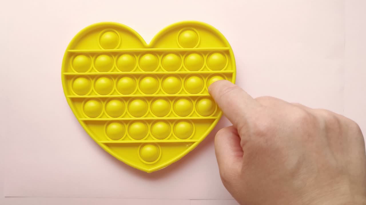 новая детская игрушка. поп-ит игра с пальцами. забавный цвет. взрослая рука сжимает круглый силикон. изменить форму. желтая форма сердца