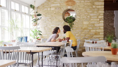 pareja de edad media de raza mixta sosteniendo las manos a través de la mesa durante una cita en un restaurante vacío