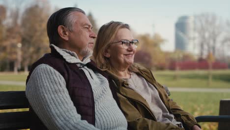 caucasian senior couple sitting at the bench at park and embracing.