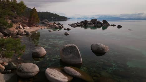 sunny shoreline mid winter day sand harbor secret beach south lake tahoe aerial drone california shoreline large boulder rocks crystal clear glassy turquoise fresh water right motion