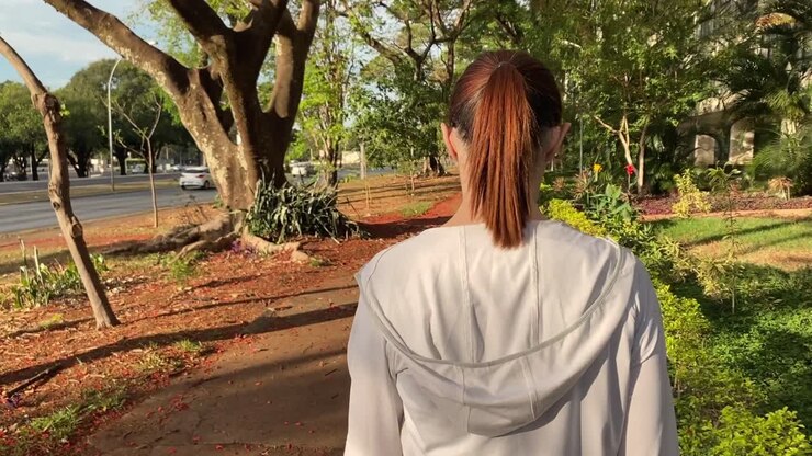 Giovane donna bruna vista da dietro che cammina in città su un marciapiede crepato e pericoloso.
