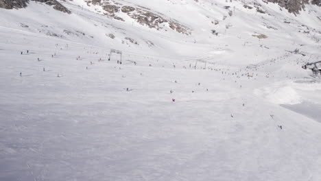 Weitwinkel-Drohnenaufnahme-Von-Menschen,-Die-An-Einem-Sonnigen-Tag-Eine-Verschneite-Skipiste-Am-Kitzsteinhorn-In-Österreich-Hinunterfahren