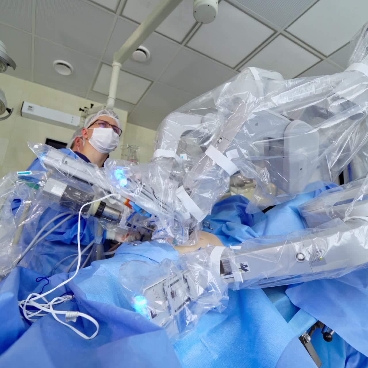 Futuristic surgery. Robotic machine with surgical arms doing minimally invasive surgery. Surgeon looks at the work of robotic machine in modern operating room
