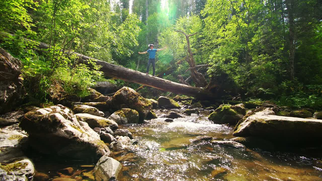 Man walking on a fallen log over a stream in a forest