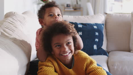 pre-teen girl lying on sofa watching tv, her younger brother sitting on her back, close up