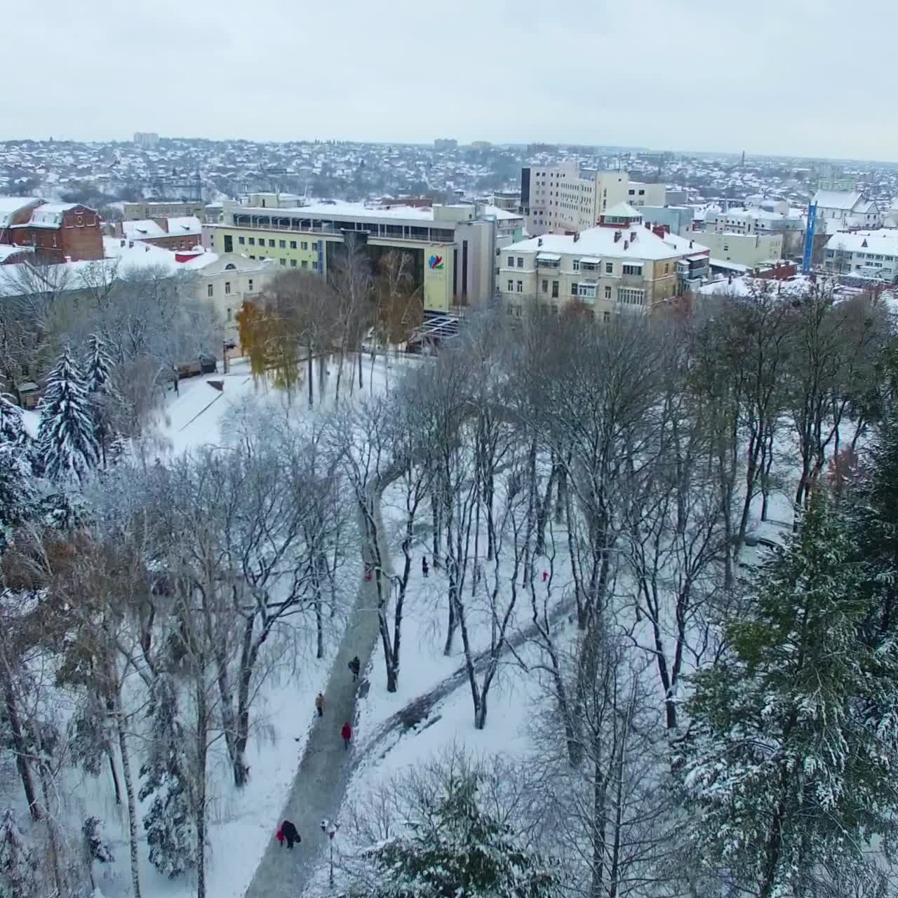 People walking by the park in winter. Amazing panorama of the city centre with old tower and diverse architecture. View from drone