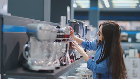 In-the-appliances-store,-a-brunette-woman-in-a-shirt-chooses-a-blender-for-shopping-by-viewing-and-holding-the-device-in-her-hands.