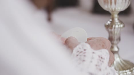 narrow depth of field tracking shot of priest's hands breaking the eucharist or sacrament