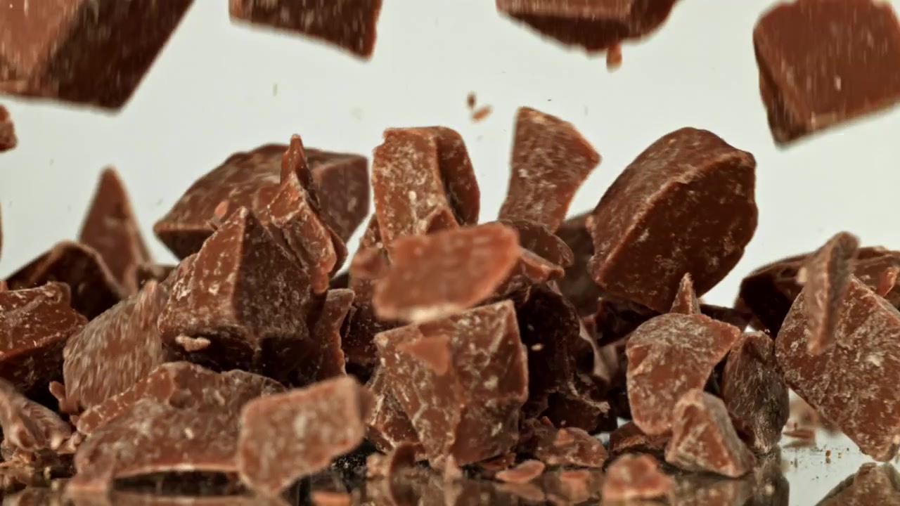 Pezzi di cioccolato che cadono al rallentatore su una superficie riflettente