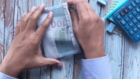 persona poniendo dinero en una bolsa en una superficie de madera