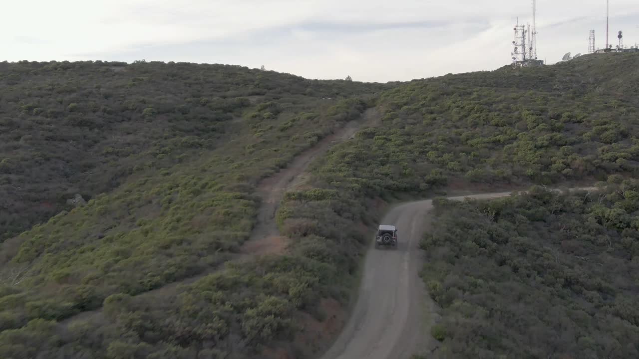 toma aérea de un jeep y un coche conduciendo por la montaña hasta el océano