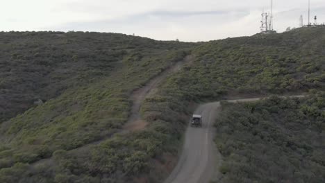 Aerial-shot-of-Jeep-and-car-driving-over-mountain-ridge-to-ocean