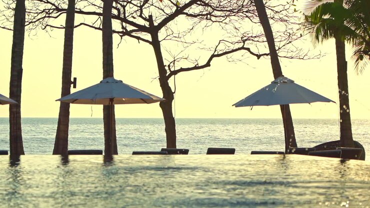 Piscina a sfioro e zona lounge con diversi ombrelloni e sedie a sdraio al tramonto, ripresa a mano libera.