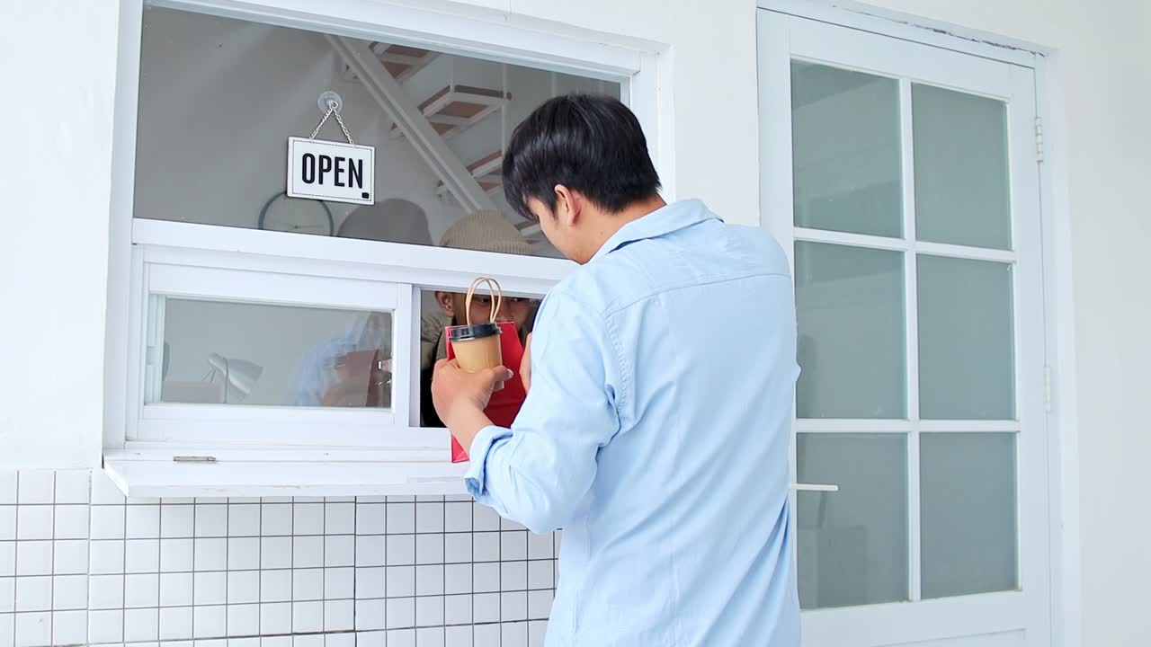 Smiling worker passing customer orders through window at cafe