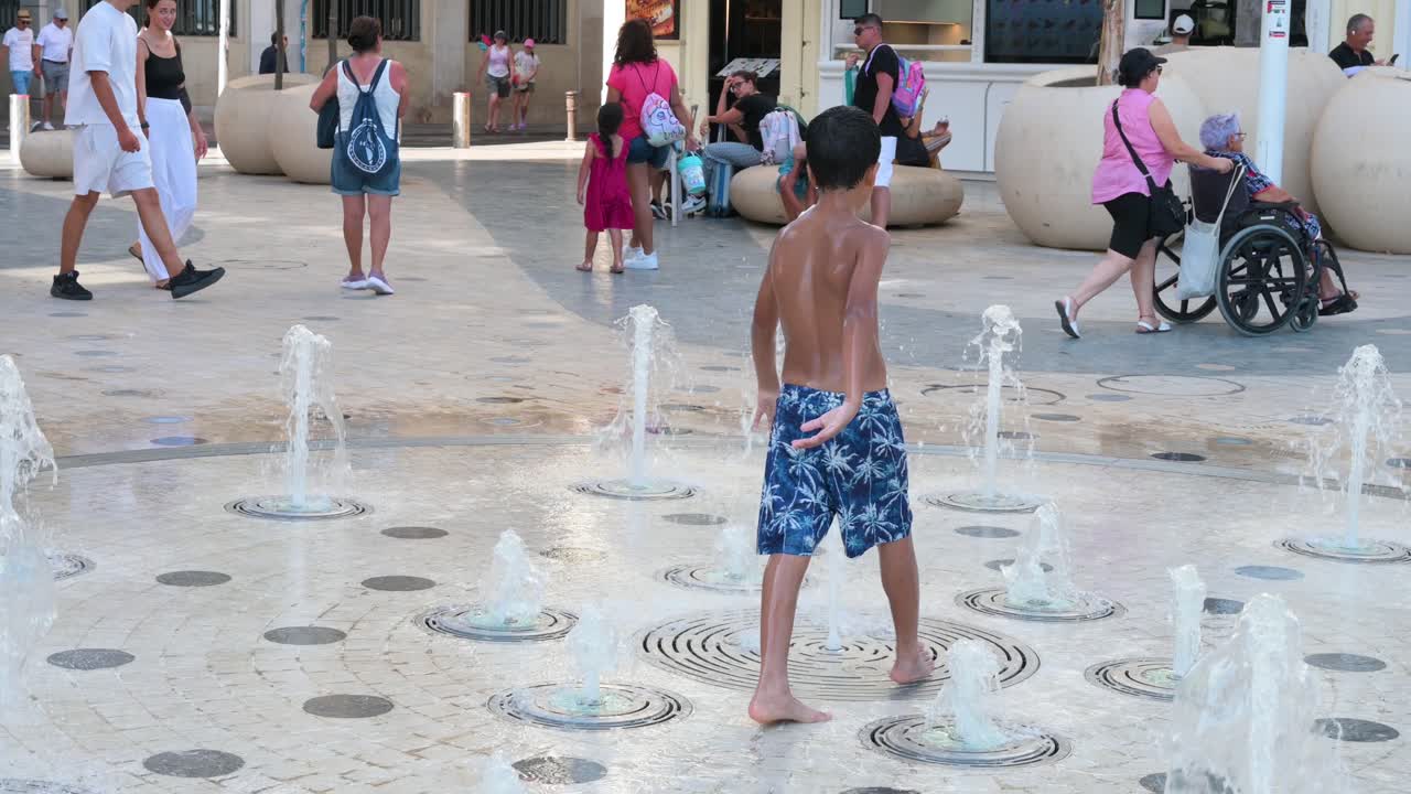 Children cool off at a street water fountain during a hot summer day near La Explanada in Alicante, Spain.