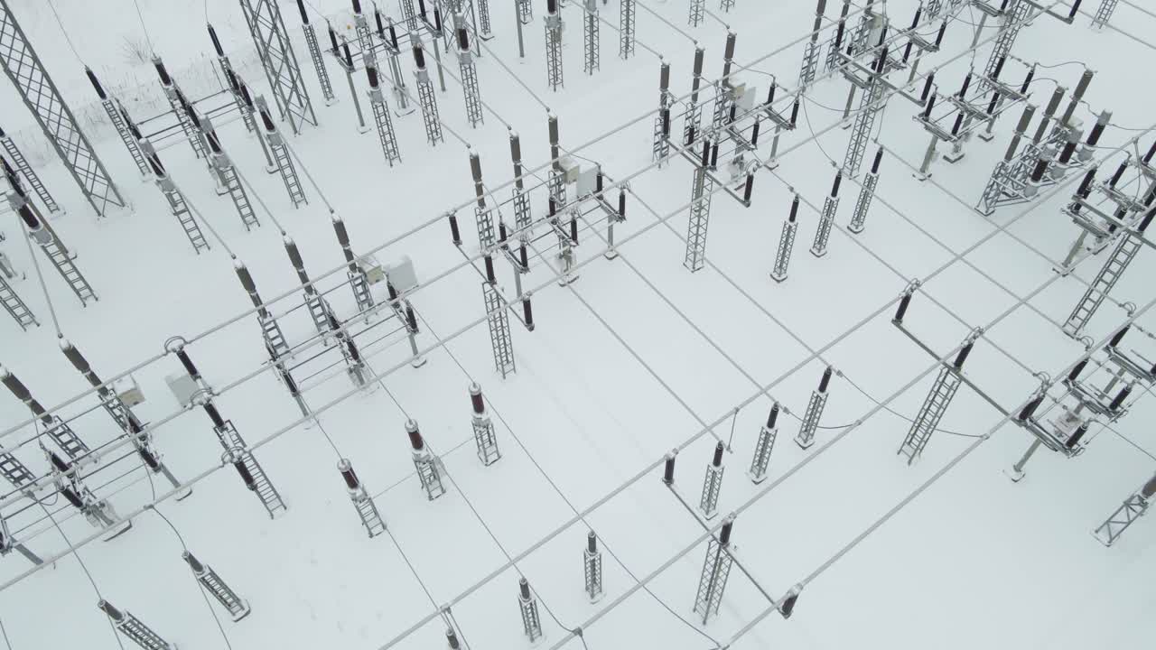 Orbita aerea a bassa quota sopra una sottostazione elettrica ghiacciata, che rivela fitte file di isolatori ad alta tensione, cavi e strutture in acciaio sepolti nella neve invernale incontaminata.