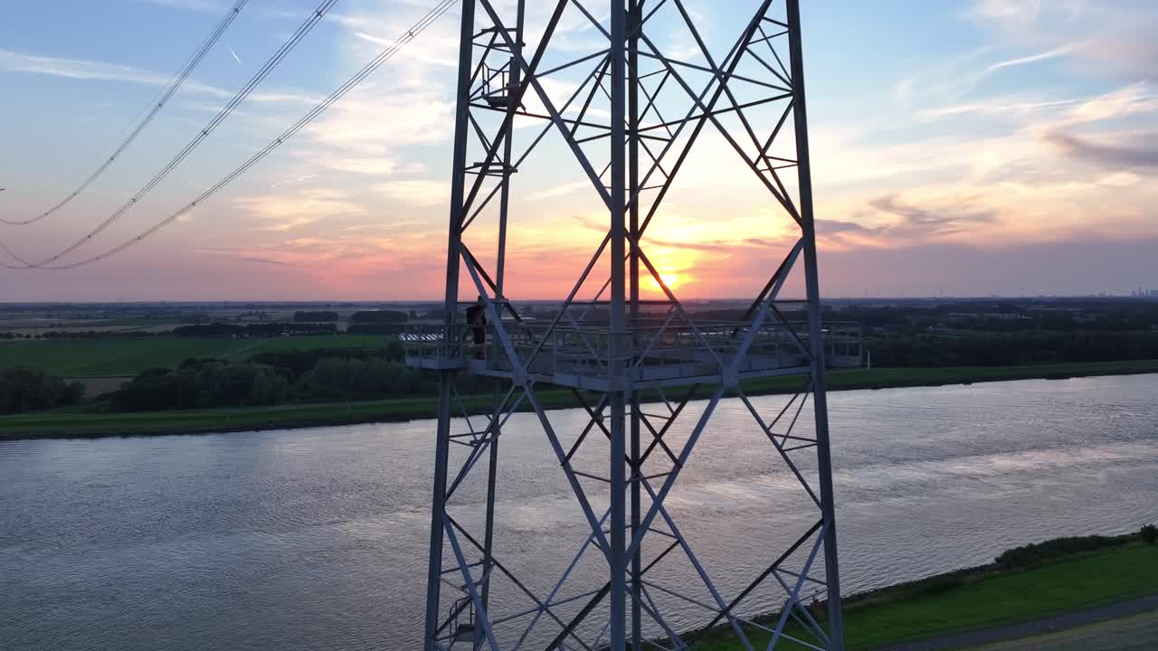 Person preparing for a base jump on a metal tower overlooking a river during sunset