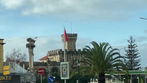 Amplia-Vista-Del-Castillo-Con-Bandera-Portuguesa-En-La-Playa-En-Estoril,-Portugal