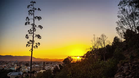 una brillante bola roja y amarilla de sol se levanta entre las nubes sobre málaga, españa