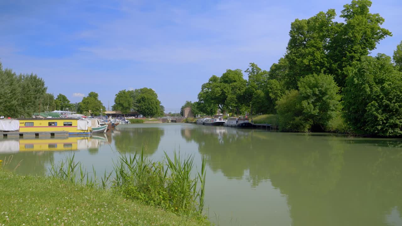 파란색 옷을 입은 젊은 금발 백인 여성, 바지와 함께 강을 마주하는 풀에 누워, 그녀의 오른쪽 팔에 검은 연결 된 시계를보고