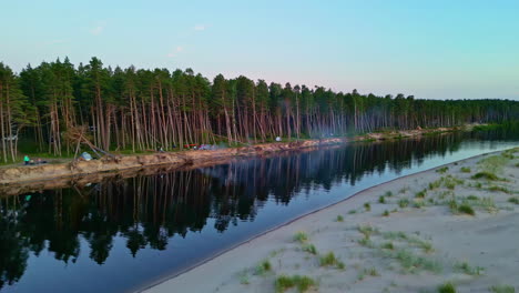 people camping by a river near a pine forest