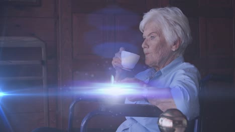 animation of light moving over smiling senior caucasian woman in wheelchair drinking tea