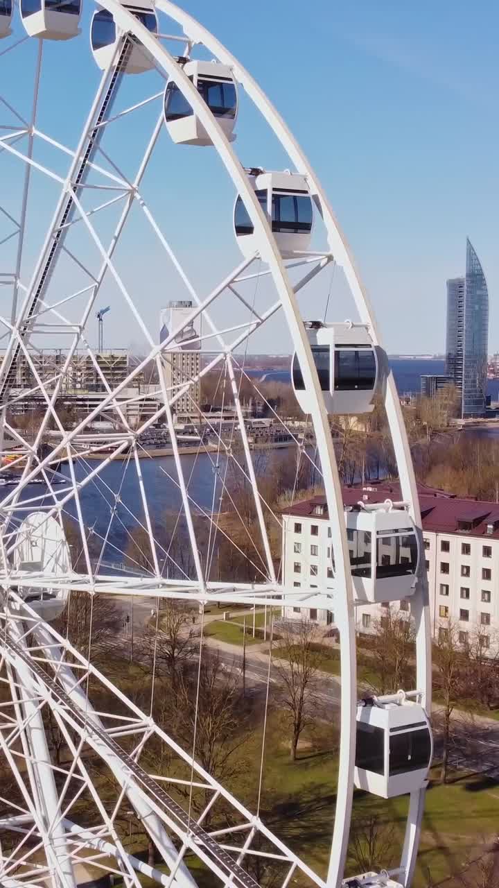 Panoramic Ferris wheel with Riga city buildings in background, aerial vertical close up